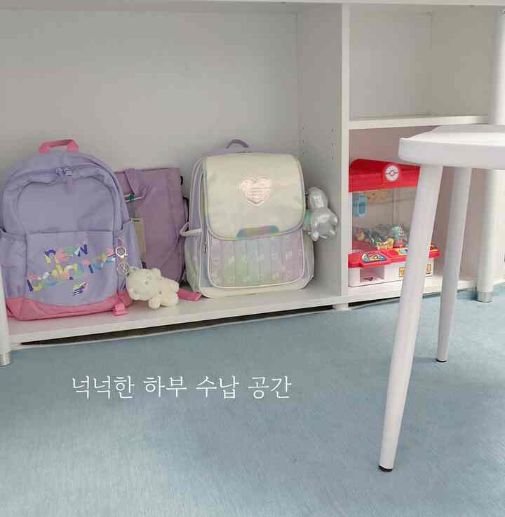 白とラベンダーの色調の子供部屋、下部の棚に子供用バッグとおもちゃが整頓された収納スペース