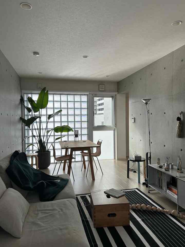 チャコールグレーのダイニング兼リビングルーム、木製ダイニングテーブルとラタンチェア、観葉植物、白いソファが配置された自然でモダンなインテリア