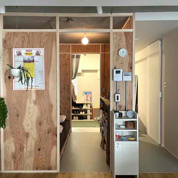 Natural wood tone and white studio apartment living room featuring structural plywood walls, a poster, and plants creating a clean atmosphere