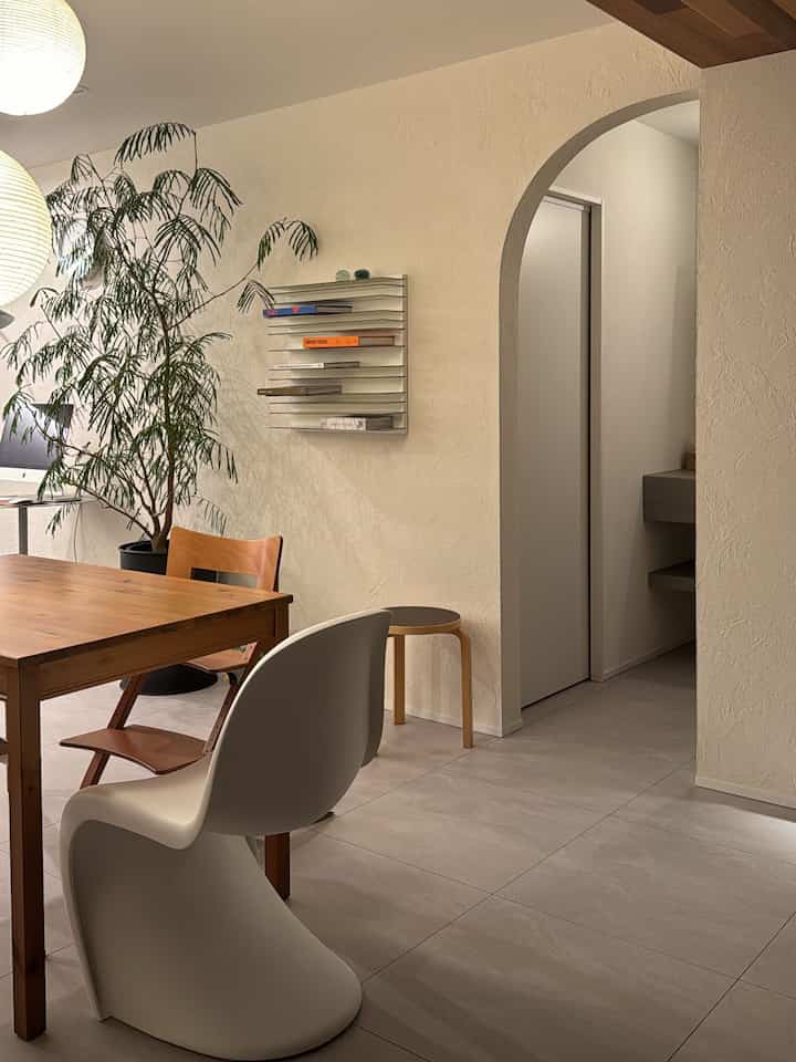 白い壁と木目調のダイニングテーブル、アーチ型の入り口があるナチュラルなダイニングルーム