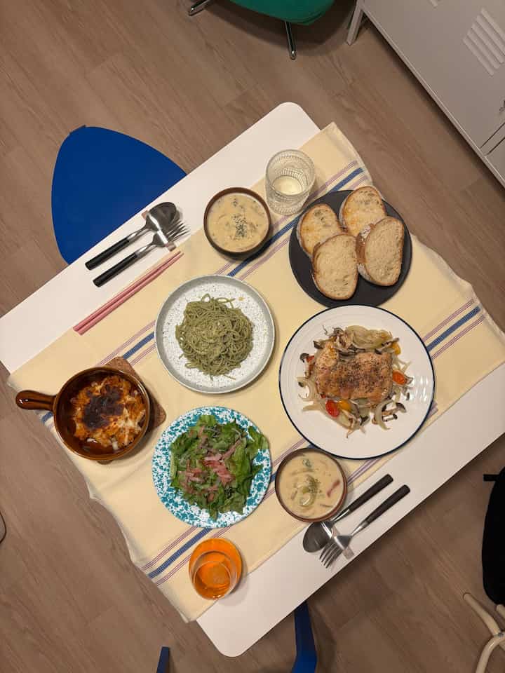 ホワイトのダイニングテーブルとウッドトーンの床にスツールが配置された二人暮らしのダイニング、家庭料理が並ぶ雰囲気のあるおうちカフェ空間