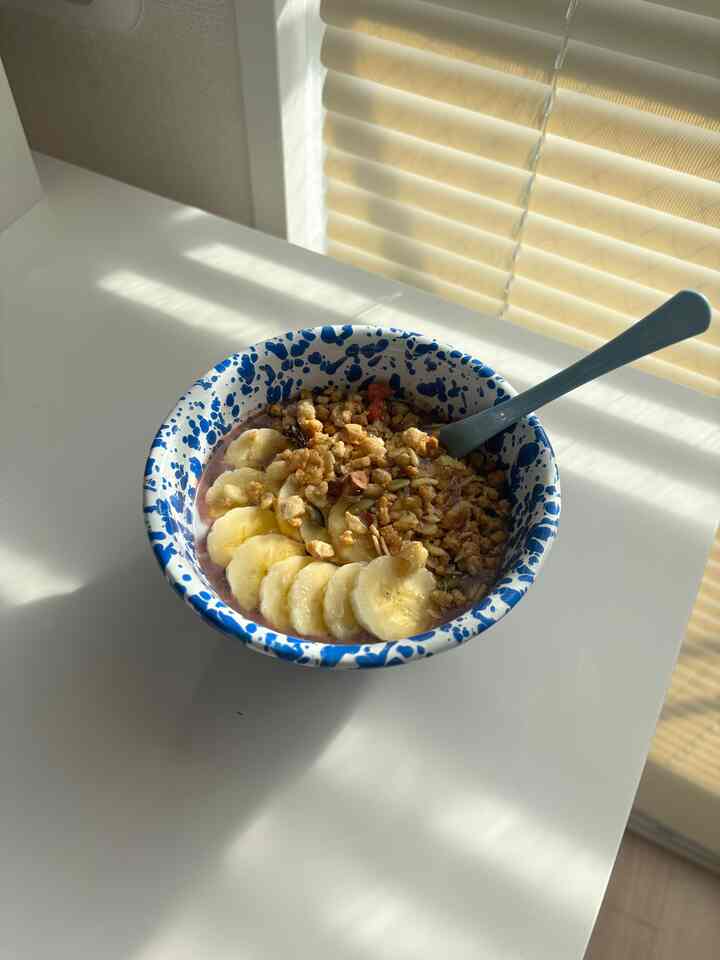 自然光が差し込むベージュのブラインドと白いダイニングテーブルにアサイーボウルが置かれた雰囲気のあるキッチン