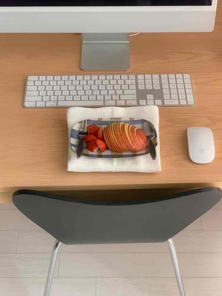 ナチュラルトーンの木製デスク上に青のストライプ模様の陶器の皿と赤い果物が置かれたシンプルな書斎の空間