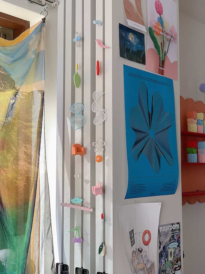 白い壁に青いポスターが貼られ、カラフルなモビールが垂れ下がる、自然でアートな雰囲気のある壁面空間