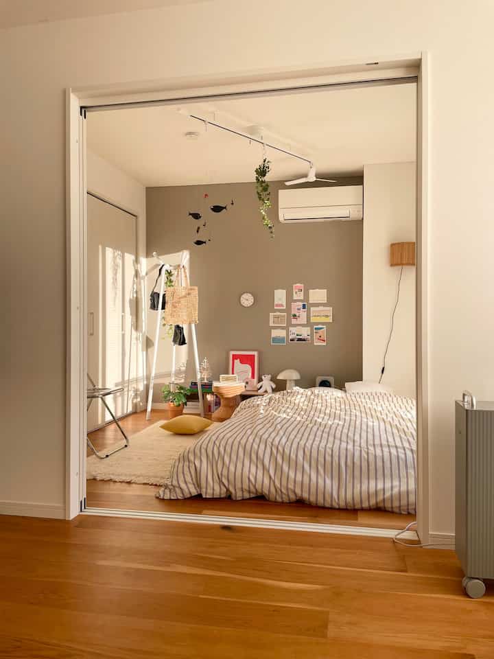 Beige and white toned bedroom featuring bed, coat rack, mobile, and poster in a cozy natural modern interior