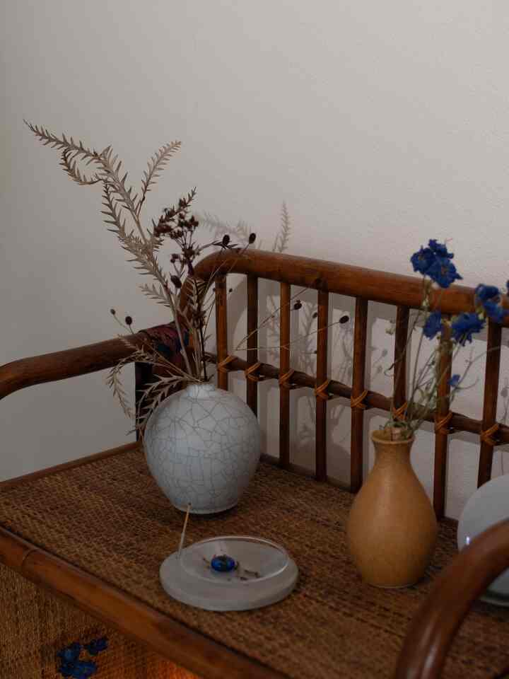 Natural-toned small space, featuring a rattan bench with white and brown vases holding dried flowers, creating a calm atmosphere