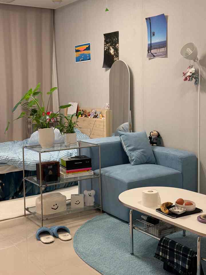 柔らかなパステルブルーとナチュラルカラーのワンルームリビング、ソファとラグ、大きな全身鏡が配置された雰囲気のある空間