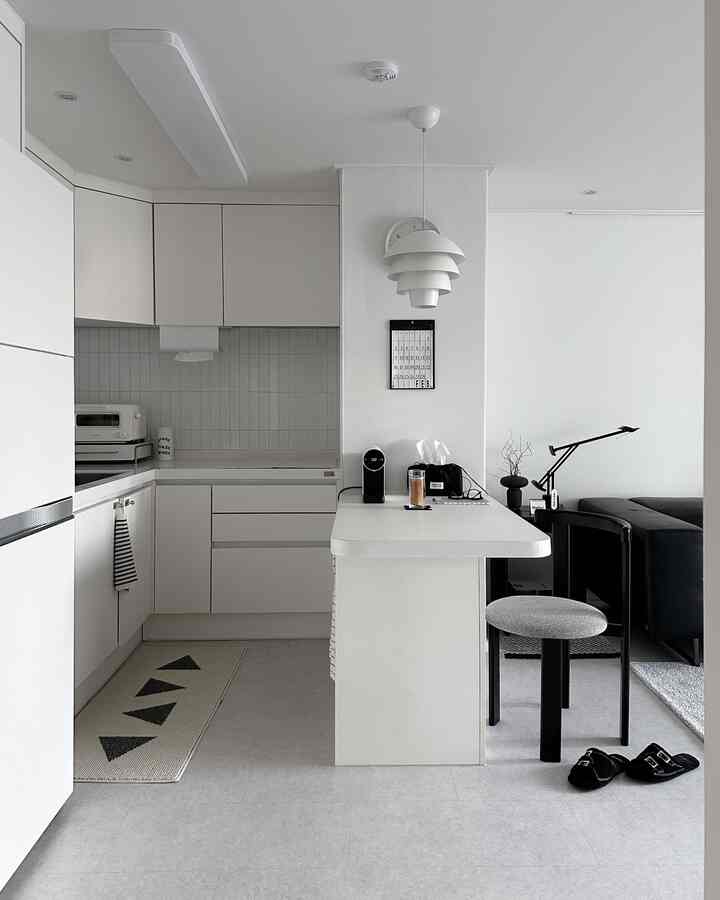 A white and monotone studio apartment kitchen featuring a simple pendant light and dining chair with a modern vibe
