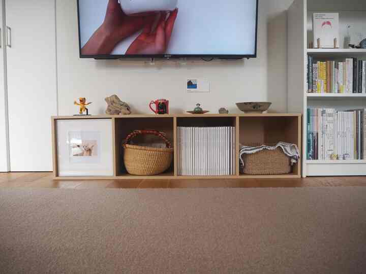 白い壁と木目調の床が印象的な北欧風のリビング、テレビ台と本棚が整然と配置された雰囲気のあるインテリア