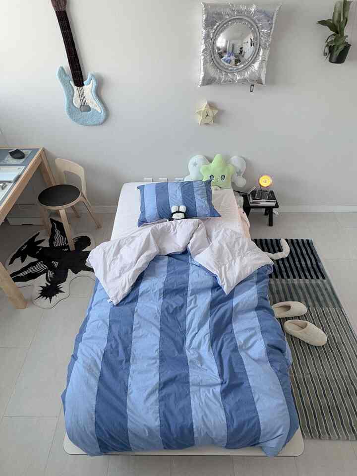 白い壁と青のストライプ寝具があるシンプルでモダンなシングルベッドルーム