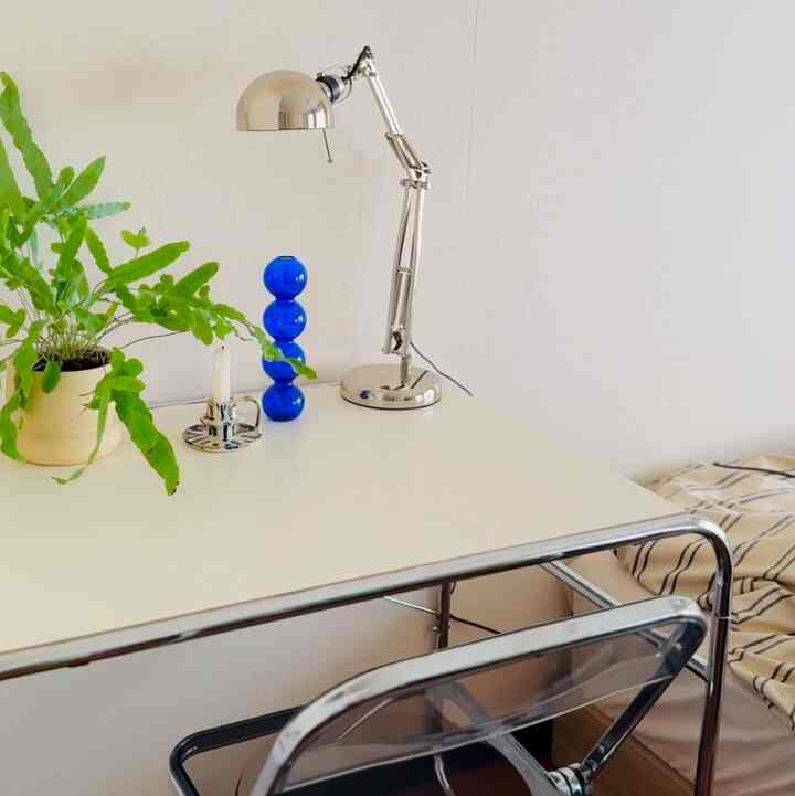 白を基調としたホームオフィス、白いデスク上に緑の植物とシルバーのテーブルランプ、青い花瓶が配されたシンプルで落ち着いたインテリア