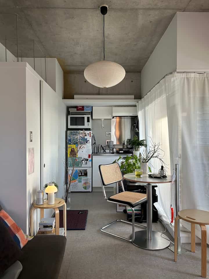 白を基調としたワンルームのキッチン兼ダイニング、木目調の家具とシンプルなペンダントライトが配置された清潔感のあるインテリア