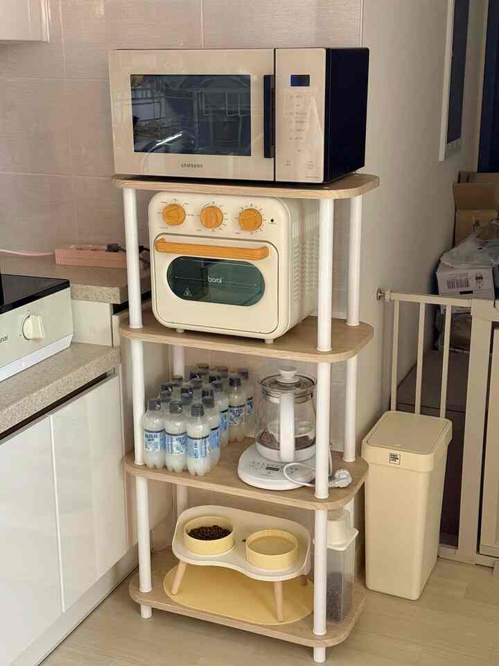 ベージュとホワイトのトーンの狭いワンルームキッチン、組み立て式収納棚に電子レンジとエアフライヤー、犬用食器が配置された実用的なインテリア