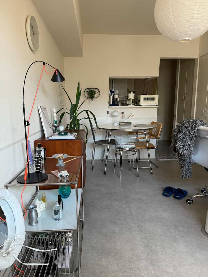 White-tone long and narrow 1LDK living and dining area featuring floor lamp, modular shelves, and wood-tone furniture in a modern interior style