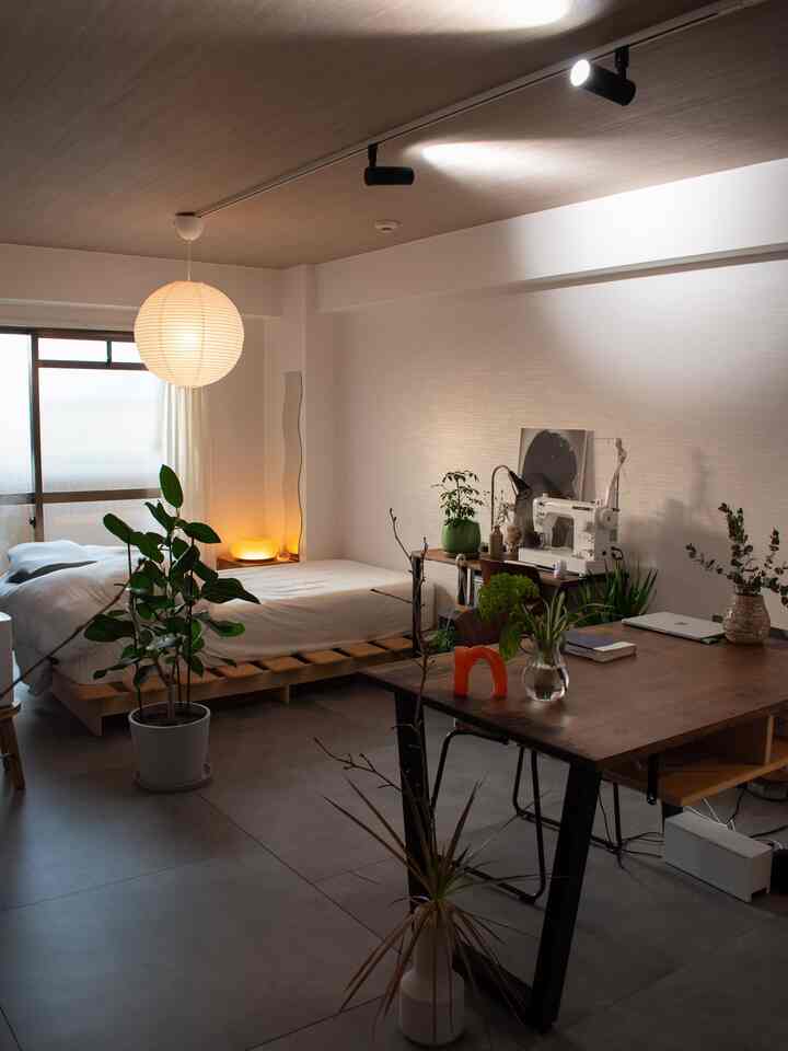 ナチュラルな木目調と白い壁のワンルーム、豊富な植物と木製テーブルが配置された温かみのあるリビング兼寝室のインテリア