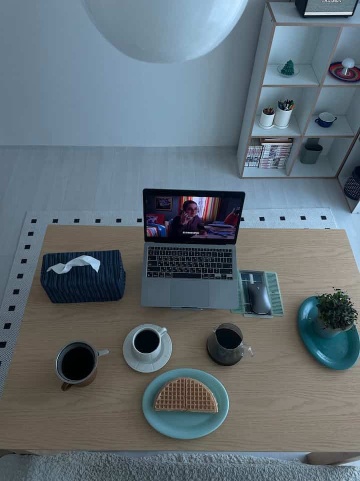 明るいブラウンのテーブルにノートパソコンとコーヒーカップ、ワッフルが配置されたミニマルで雰囲気のあるホームカフェ風ホームオフィス