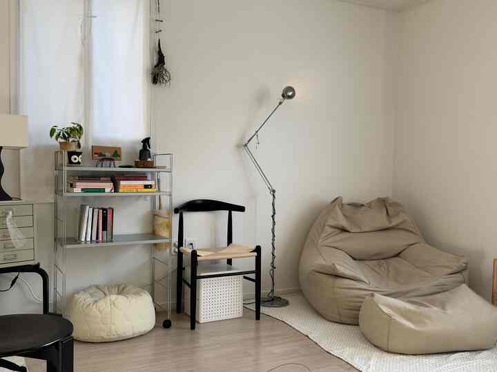 ナチュラルでベージュトーンの一人暮らしのリビング、ビーズクッションソファとスツール、棚が配置されたミニマルで落ち着いた空間