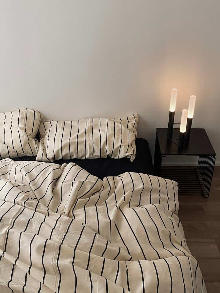 Beige and black toned bedroom featuring striped bedspread and table lamp, clean and warm atmosphere