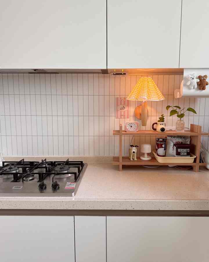 A simple kitchen featuring white and wood tones with a yellow gingham table lamp and retro clock arranged neatly on the countertop