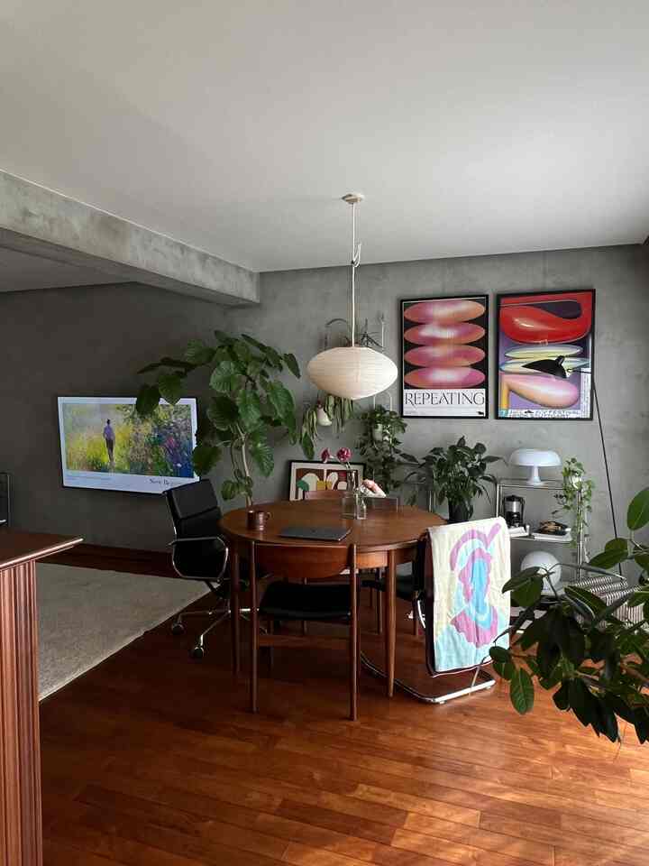 グレーの壁と木目調の床、ミッドセンチュリーモダンのリビング、植物とアートポスターが配置された雰囲気のある空間