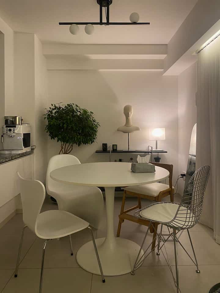 白とグレーのトーンのダイニングルーム、丸テーブルと様々な椅子が配置されたミッドセンチュリーモダンの印象的な空間