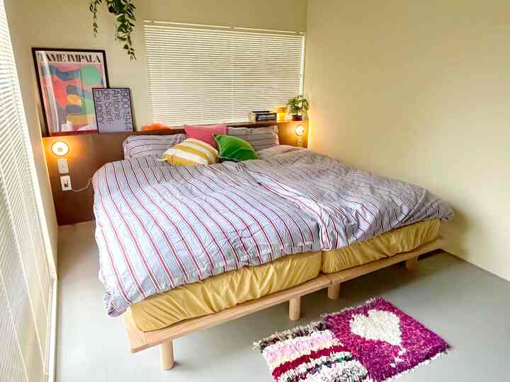 イエローとホワイトのトーンの寝室、ストライプのベッドカバーとカラフルなクッションが配置されたナチュラルモダンなインテリア