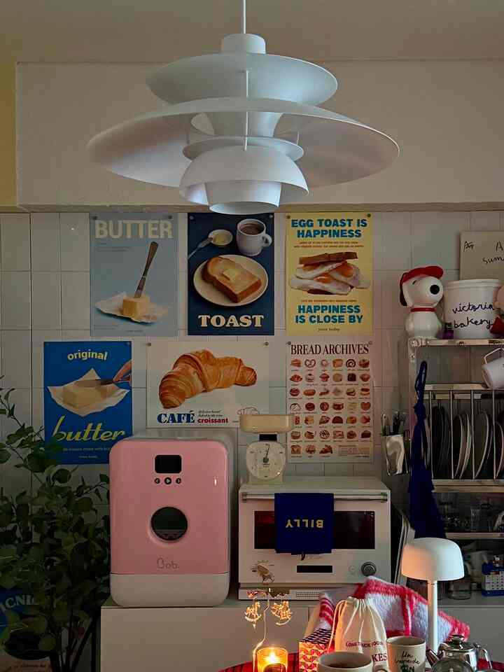 白いタイルの壁とピンクの「Bob.」キッチン家電があるダイニングルーム、パンのポスターが並び、落ち着いたホームカフェの雰囲気の空間