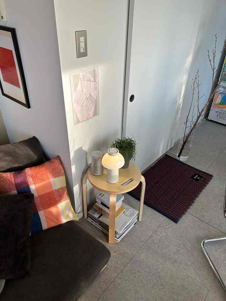 Natural-tone studio apartment living room featuring a dark brown single sofa and wooden stool with table lamp, creating a cozy atmosphere