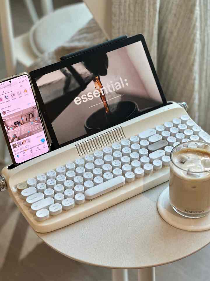 ホワイトとベージュの色調が特徴のホームオフィス空間、ヴィンテージ風キーボードとタブレット、アイスコーヒーが置かれたコンパクトな作業スペース
