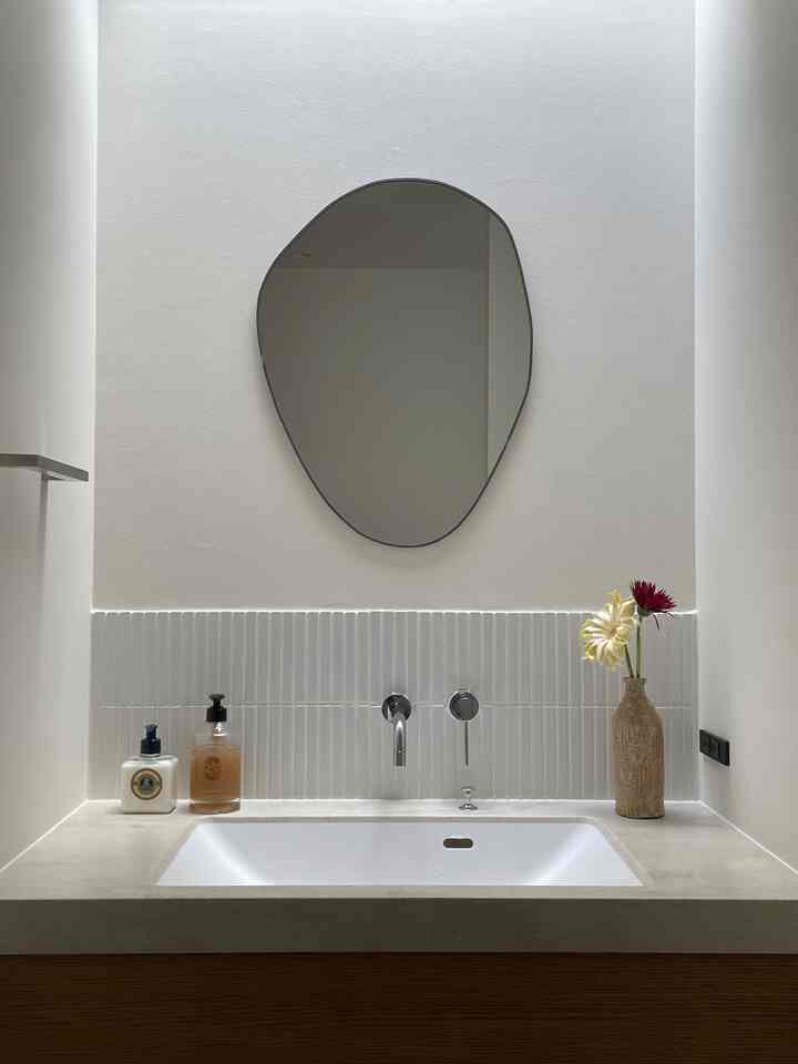 White and wood-tone bathroom sink area with an irregular mirror and minimal decorative elements creating a calm interior