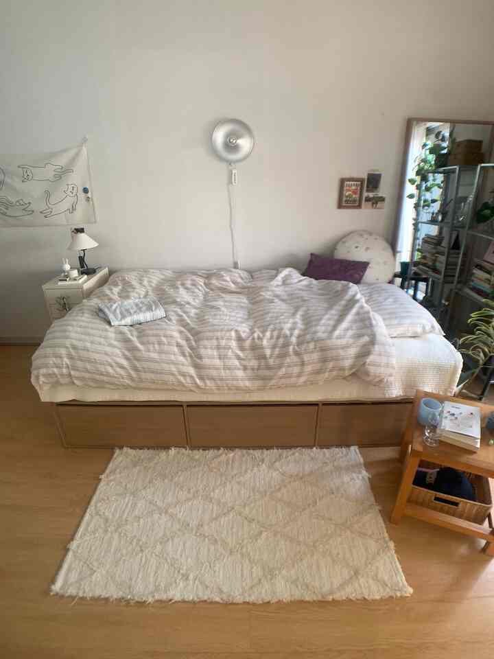 白と木目調でまとめられた8坪のワンルーム寝室、ベッドと収納引き出し、サイドテーブル、植物が配置された自然な雰囲気のインテリア