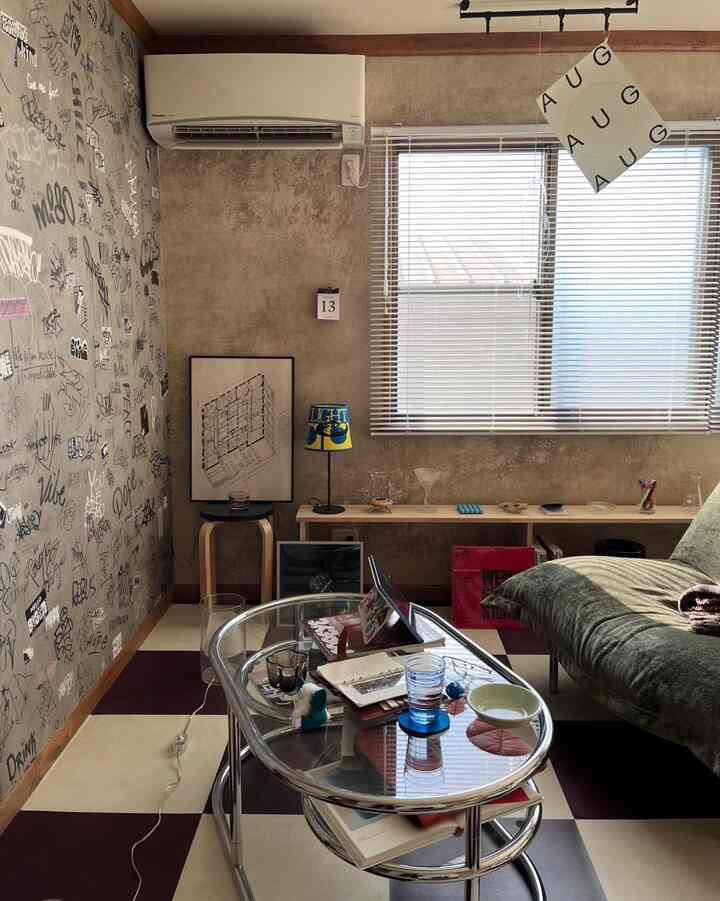 レトロな雰囲気の狭いリビング、グラフィティ壁紙とグリーンのソファ、ガラスのコーヒーテーブルが配置された印象的なインダストリアルインテリア