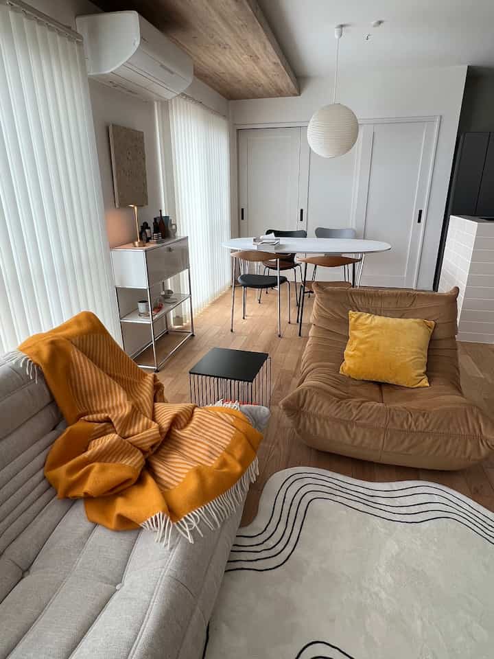 Natural tone wooden floor and white walls in a Mid-Century Modern living room, featuring orange throw blanket and cushion creating a cozy space