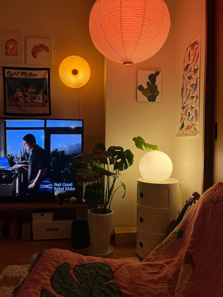 暖かいオレンジ色のペンダントライトと白い球形のテーブルランプが配置された雰囲気のあるリビング