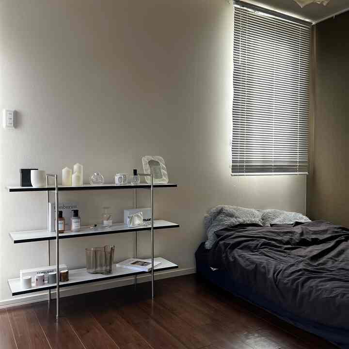 ナチュラルな色調のワンルーム、無印良品のベッドカバーと3段の棚が配置された落ち着いた雰囲気のあるインテリア