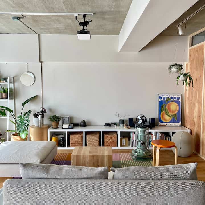 Natural style living room with white walls and wood tones, featuring sofa, stool, and various indoor plants creating a cozy atmosphere