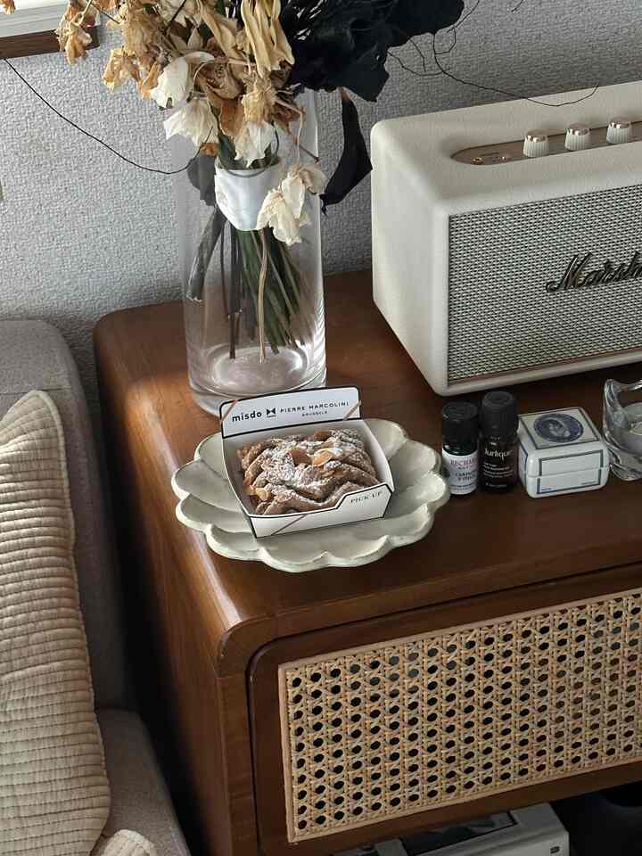 ブラウンウッド調のリビングのナイトテーブルにドライフラワーとミスド ピエールマルコリーニのペストリーが置かれた、自然でシンプルな雰囲気のインテリア