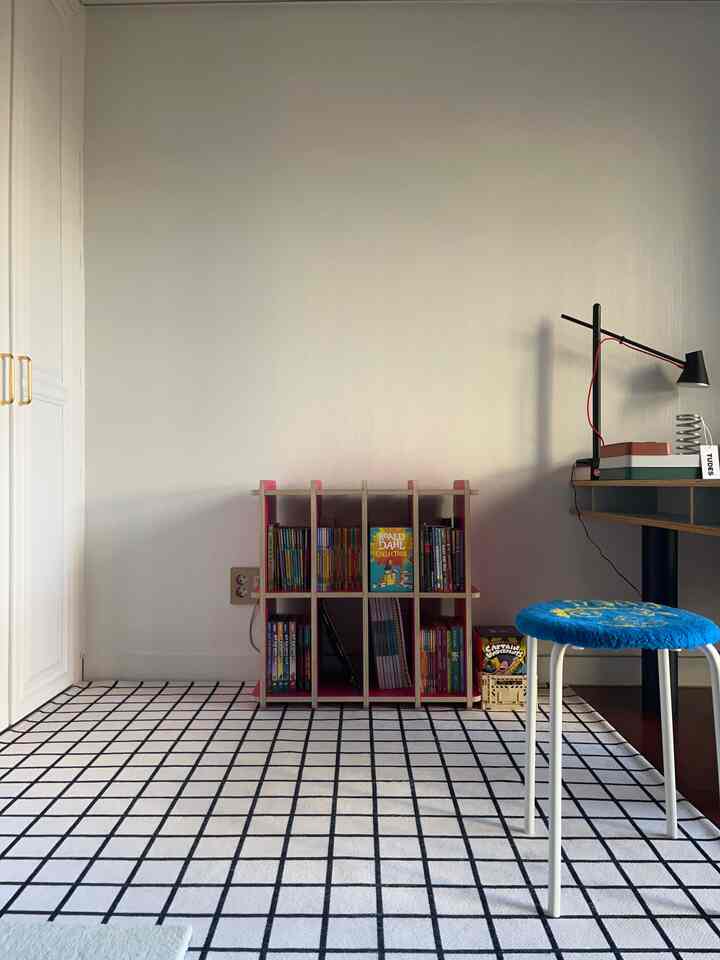 A 4.5-tatami size room featuring white and black grid rug, center bookshelf, and right-side desk with blue stool in an orderly interior space