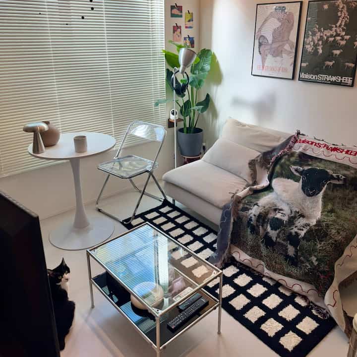 白とシルバーの落ち着いた雰囲気のリビング、ソファと透明チェア、ブラインドが配置された印象的な空間