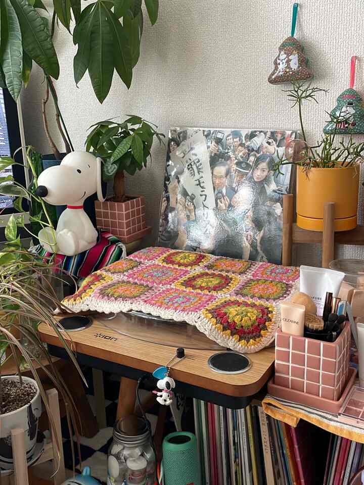 白い壁と茶色の木製家具がある一人暮らしのカフェ風インテリア、多数のインドアグリーンとビンテージのレコードプレーヤーが配置された雰囲気のある空間