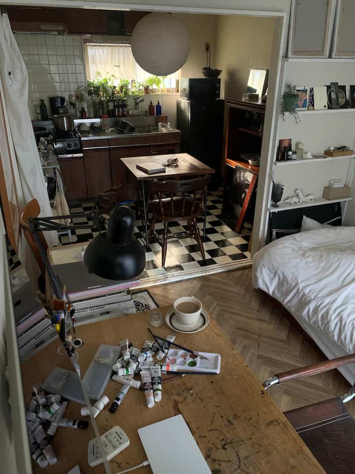 ナチュラルな色調の一人暮らし用ワンルーム、ヴィンテージ家具と植物が配置された雰囲気のある散らかった空間