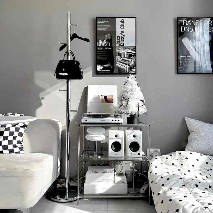 グレートーンの壁にホワイトソファ、ドット柄の寝具、クローム素材のスタンドハンガーとターンテーブルが配置されたモダンなワンルーム寝室のインテリア