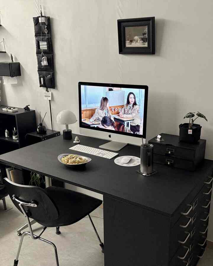 モノトーンのホームオフィス、黒いデスクと椅子、モニター、額縁が配置されたすっきりとした作業空間