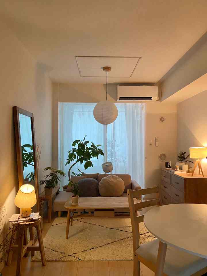 ナチュラルカラーと木目調が調和した居心地の良いリビング、ソファ、大きなテーブル、ラグ、キャビネットと植物が配置された落ち着いた空間