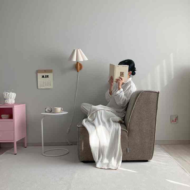 White and beige toned living room featuring a single sofa, side table, and wall sconce creating a cozy ambiance