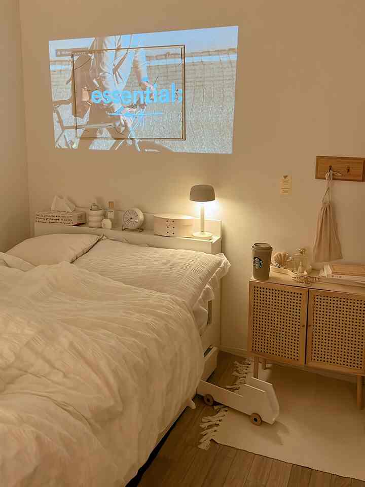 White and natural toned bedroom featuring a bed and a projector casting video on the wall, creating a cozy atmosphere
