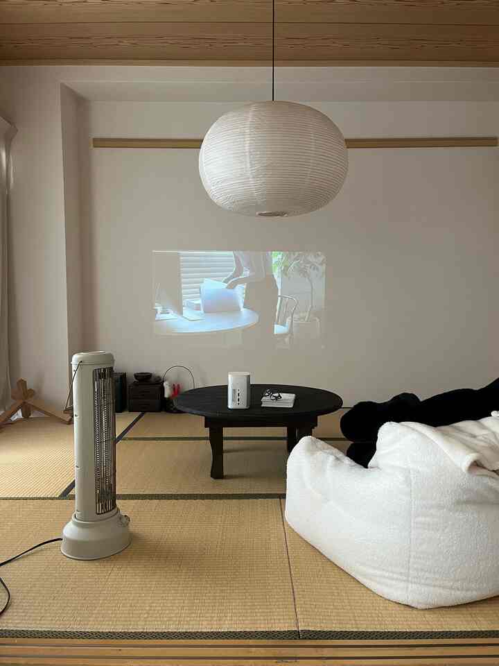 Natural tone compact Japanese-style room with tatami flooring, white tofu-style single sofa, central round table, and pendant light, cozy single living space