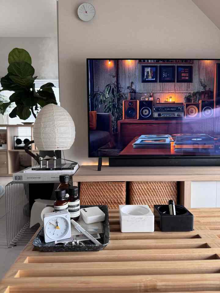 ナチュラルな色調のリビング、テレビ台と木製テーブル、時計とテーブルランプが配置された清潔感のある空間