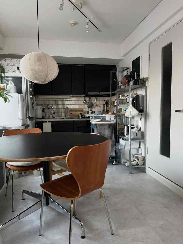 白い壁と黒のキッチン家具、木目調のダイニングチェアが配置されたコンパクトな一人暮らしのダイニングルーム