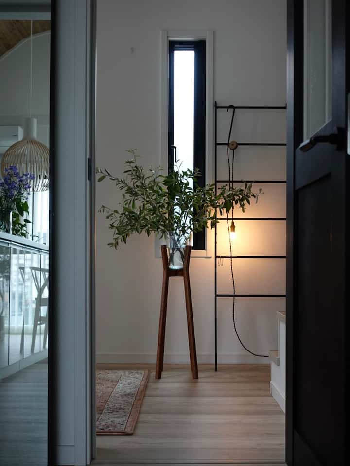 ナチュラルな色調の玄関、木目調の床と木製の植物スタンドが配置された落ち着いた空間
